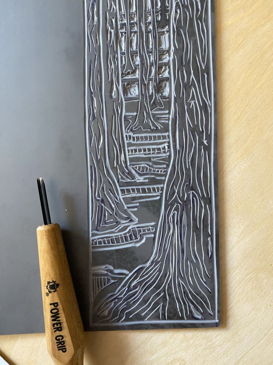 A linoleum block carved with redwood trunks, a wooden carving gouge resting beside it