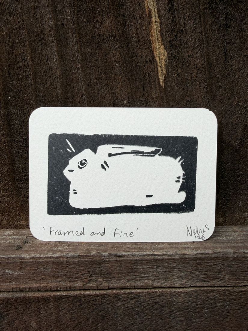 A tiny linocut print of a rabbit inside a black rectangle, titled Framed and Fine, standing on weathered wood