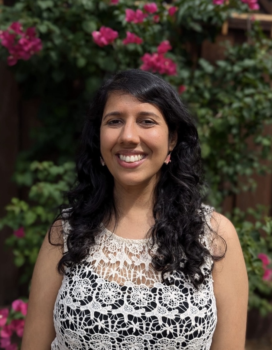 Neha Srivastava smiling in front of a blooming pink bougainvillea